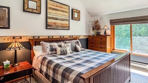 Un dormitorio con una cama grande, una mesita de noche, un aparador y una ventana con vistas al verdor.