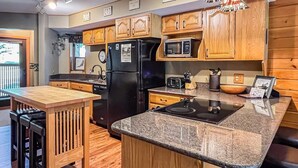 Una cocina con armarios de madera, un refrigerador negro, un microondas, un lavamanos y una encimera de granito.