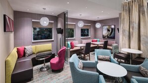 A modern lounge area with a sofa, chairs, and tables, featuring a glass partition, pendant lights, and artwork on the walls. - Residence Inn by Marriott Spartanburg Westgate (Spartanburg)