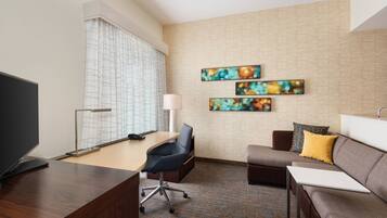 A modern hotel room with a wooden desk, a comfortable sofa, a small armchair, and a flat-screen TV.