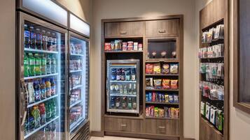 Een zone voor zelfbediening met gekoelde drankautomaten en planken vol snacks en dranken.