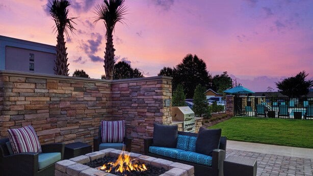 An outdoor patio with a fire pit, wicker furniture, and a stone wall. - Residence Inn by Marriott Spartanburg Westgate (Spartanburg)