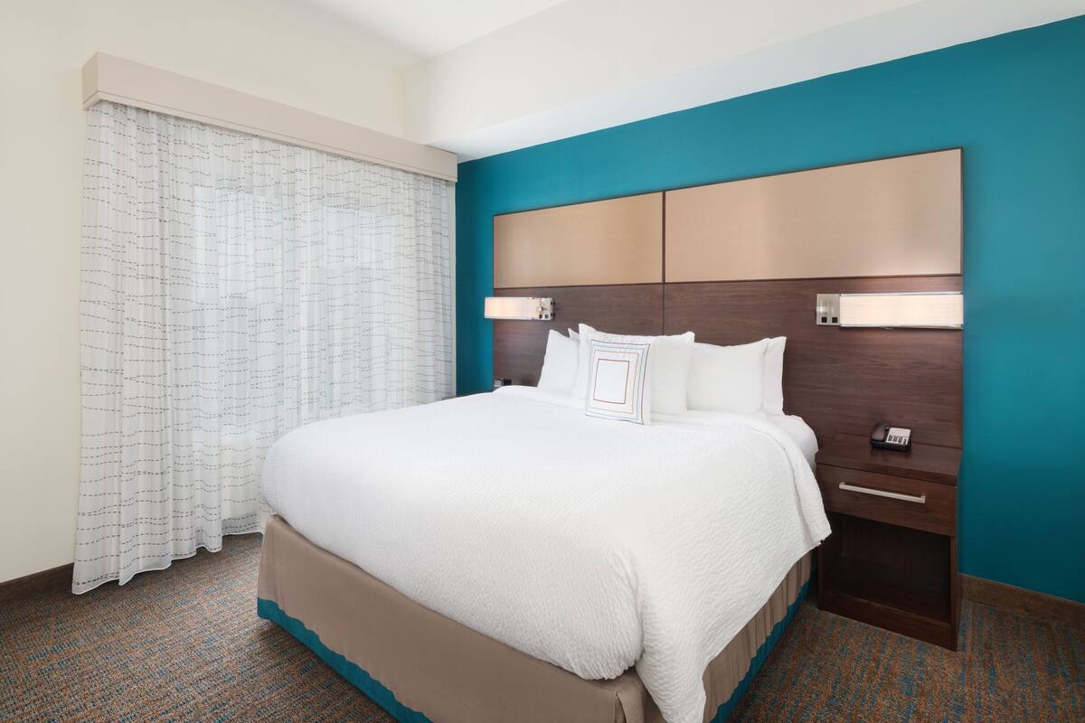 A hotel room with a large bed, a nightstand, a telephone, and a window with curtains.