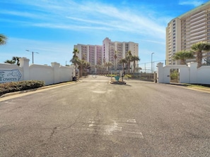 A gated residential area with a clear sky, palm trees, and a multi-story building in the background. - Pelicans Nest 3 bed 2 bath (Navarre Beach)