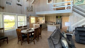 A spacious living area with a dining table, a gray sofa, and a kitchen in the background. - Hope Town harbor period home with lighthouse view (Hope Town)