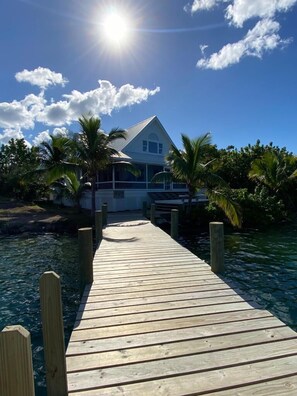A wooden dock leading to a house with a white roof, surrounded by palm trees and clear blue water. - Hope Town harbor period home with lighthouse view (Hope Town)