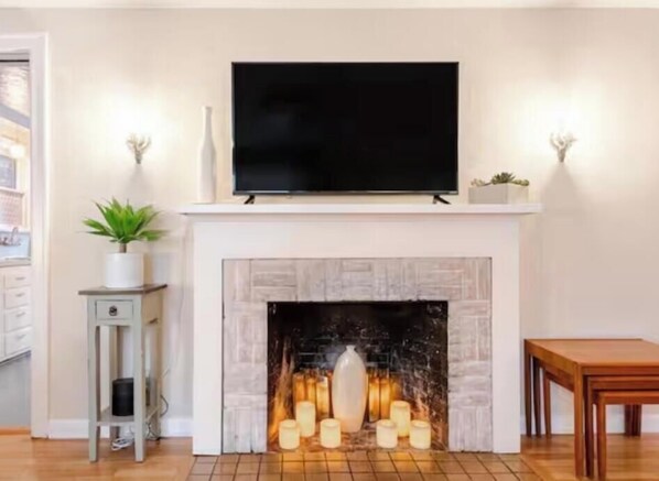 A living room with a fireplace, a flat-screen TV mounted above it, and a small table to the right.