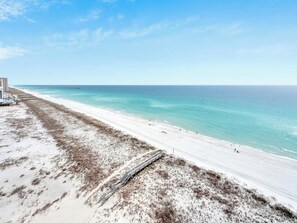 Uma praia com uma extensa faixa de areia branca, um píer ao longe e um céu azul límpido.