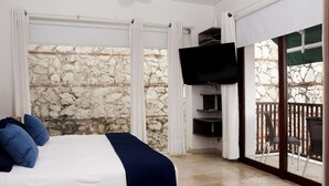 Un dormitorio con cama, televisión y balcón con paredes de piedra.