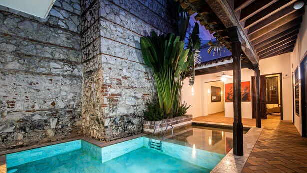 Una piscina con pared de piedra y pérgola de madera.