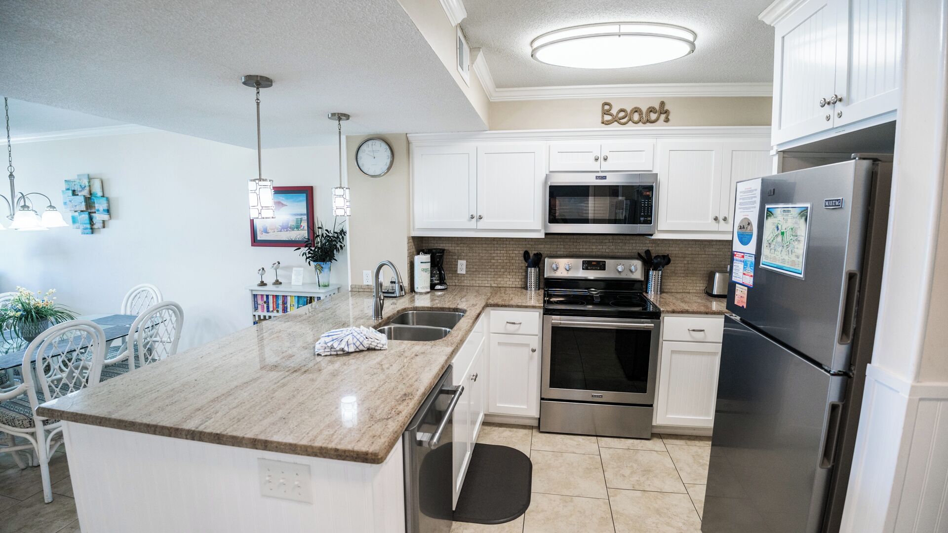 A modern kitchen with white cabinets, stainless steel appliances, a granite countertop, and a dining area with white chairs.