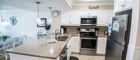 A modern kitchen with white cabinets, stainless steel appliances, a granite countertop, and a dining area with white chairs.