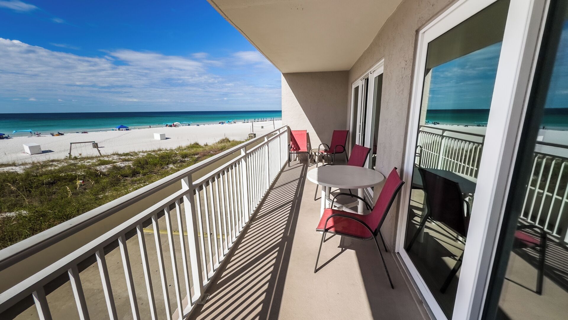 A balcony with a table and chairs, overlooking a beach with people and umbrellas.