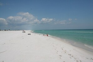 A wide sandy beach with clear turquoise water and a few people in the distance.