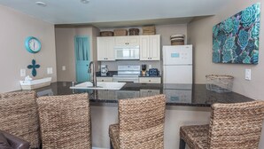 A modern kitchen with white cabinets, a central island with a sink, and wicker chairs.
