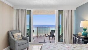 A hotel room with a bed, a chair, a desk, a lamp, and a view of the ocean. - E804 Balcony overlooks the beach! 3 Pools (Panama City)