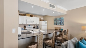 A kitchen with white cabinets, a microwave, a stove, and a sink. There are wicker chairs and a table with a woven basket. - E804 Balcony overlooks the beach! 3 Pools (Panama City)