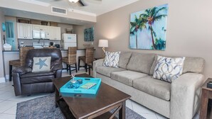 A living room with a brown leather sofa, a grey sofa, and a coffee table with a blue tray. There is a kitchen in the background with white cabinets and a microwave.