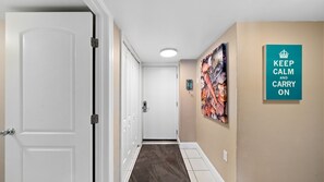 Un pasillo con puertas blancas, piso de baldosas y un cartel que dice 'KEEP CALM AND CARRY ON' en la pared.