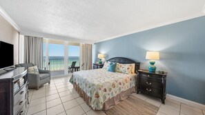 A hotel room with a bed, a TV, a desk, and a chair. There is a view of the ocean through the windows. - E804 Balcony overlooks the beach! 3 Pools (Panama City)