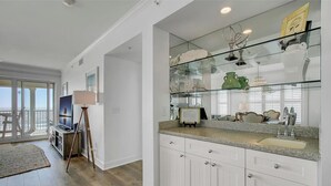 A modern kitchen with white cabinetry, a granite countertop, and a glass-fronted display case with decorative items.
