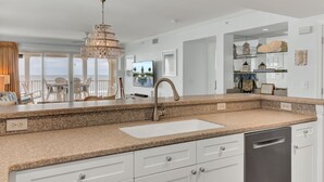 A modern kitchen with granite countertops, a stainless steel sink, and white cabinetry.