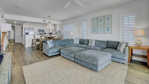 A spacious living room with a large sectional sofa, a chandelier, and artwork on the walls.