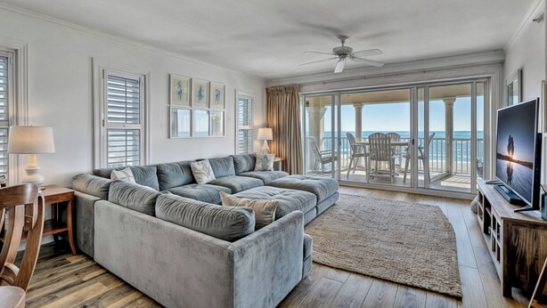 A modern living room with a grey sectional sofa, a flat-screen TV, and a large window overlooking the ocean.