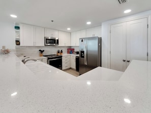 A modern kitchen with white cabinetry, stainless steel appliances, and a central island with a sink. - Sea Me Smile at Beautiful Belle Mer. (Navarre Beach)