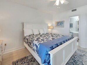 A bedroom with a bed, a nightstand, a lamp, and a door leading to a bathroom.
