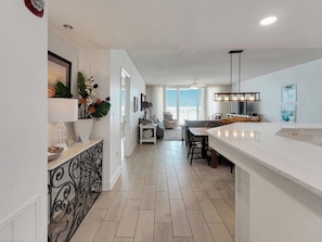 A modern kitchen with a large island, a dining area with a table and chairs, and a living room with a sofa and a coffee table. - Sea Me Smile at Beautiful Belle Mer. (Navarre Beach)