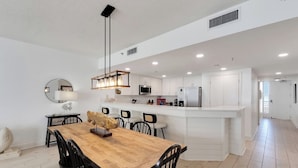 A modern kitchen with white cabinets, a central island, and a dining area with a wooden table and chairs.