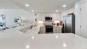 A modern kitchen with white cabinetry, a large island, stainless steel appliances, and a round mirror.