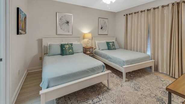 A bedroom with two beds, a ceiling fan, and a patterned rug.