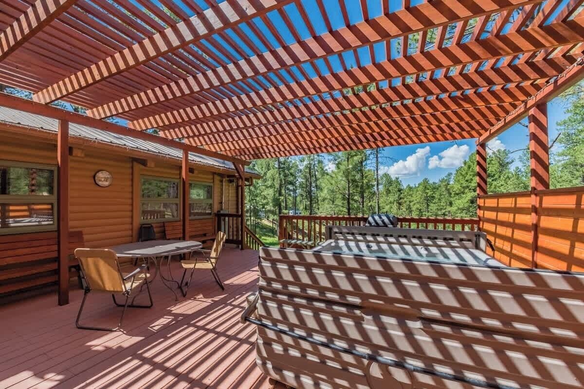 Una terraza de madera con una pérgola, una mesa con sillas y vistas al bosque.