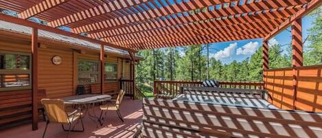 Una terraza de madera con una pérgola, una mesa con sillas y vistas al bosque.