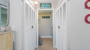 A hallway with white louvered closets, a sign above reading "Life is good at the beach", and a small rug on the floor.