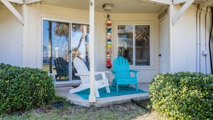 A covered porch with two white Adirondack chairs, a teal mat, and a row of colorful balls.