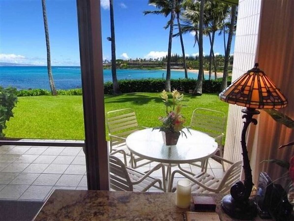 A dining area with a view of the ocean, a round table, chairs, and a lamp.