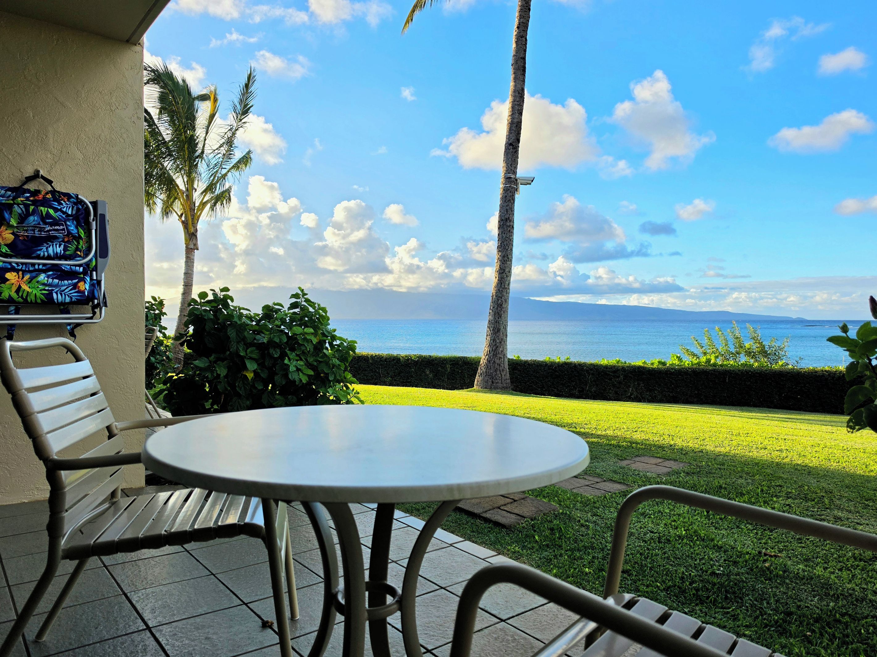 An outdoor patio with a table and chairs, a hanging bag, and a view of the sea.