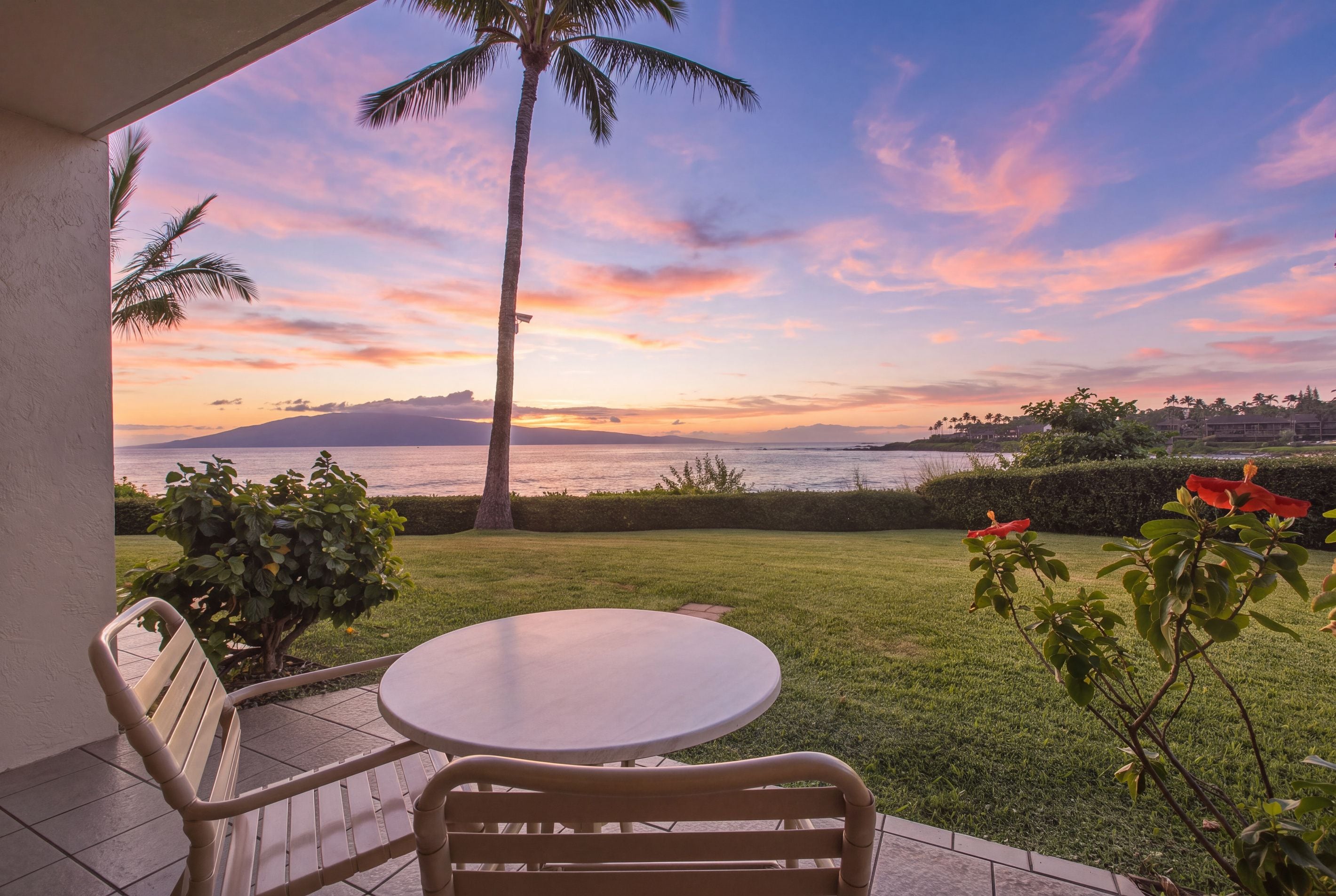 Pátio com mesa e cadeiras, com vista para a água e um pôr do sol.