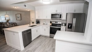 A modern kitchen with white cabinetry, stainless steel appliances, and a central island. - D506 Corner unit, 2 balconies, Fantastic view of Pool and Gulf (Panama City Beach)