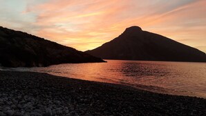 Una playa de guijarros con una montaña al fondo y una puesta de sol sobre el agua.