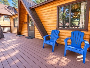A log cabin with a deck, two blue Adirondack chairs, and a door with a sign.
