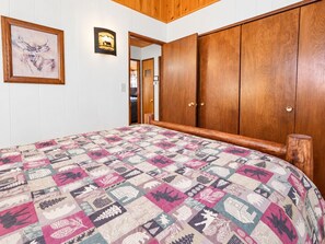 A bedroom with a wooden wardrobe, a quilt with animal patterns, and a framed picture on the wall.