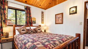 A cozy cabin-style room with a wooden bed frame, a quilted bedspread, and a window with curtains.