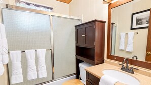 A bathroom with a shower, toilet, sink, and wooden cabinets.