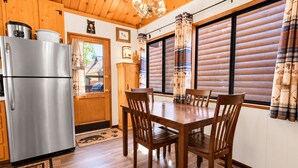 A wooden interior with a stainless steel refrigerator, a dining table with chairs, and a window with curtains.