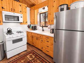 A kitchen with wooden cabinets, a stainless steel refrigerator, a stove, a microwave, and a window with a view.