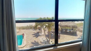 Vista de una playa desde una ventana con piscina, palmeras y una estructura de techo de paja.